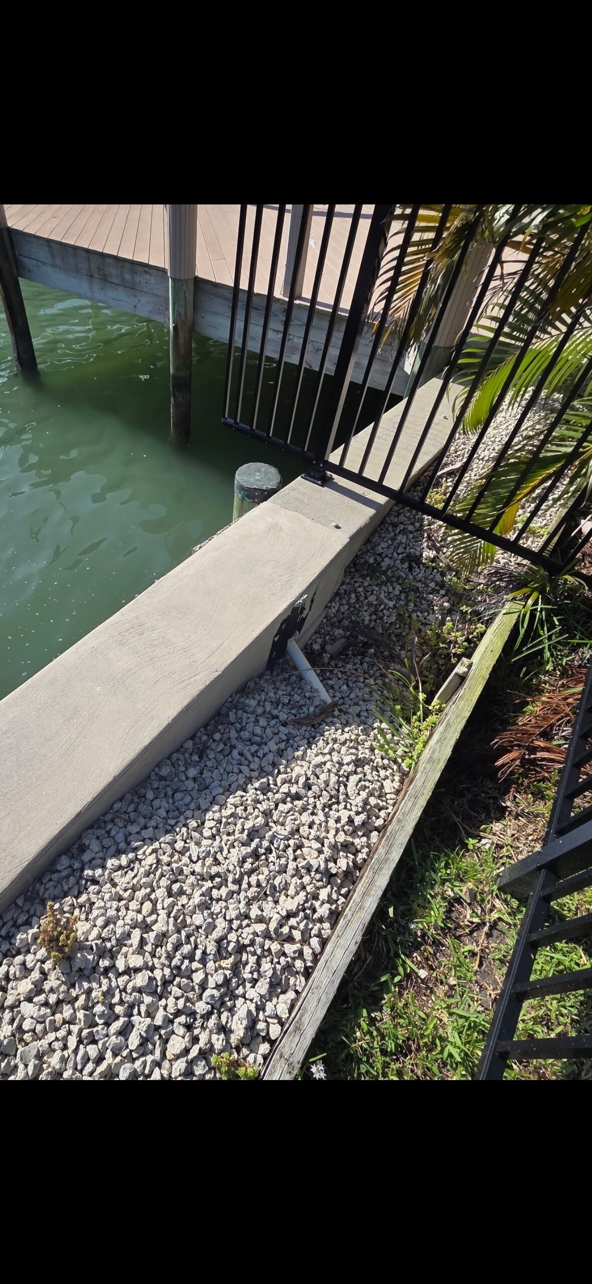 Another view of the same failure pattern — soil migrating through a crack in the seawall panel, pulling the yard down toward the water one storm at a time.