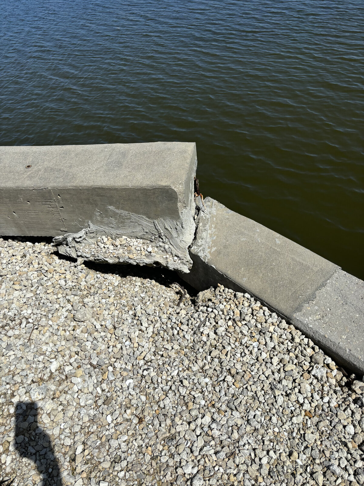 Broken seawall cap corner with concrete blown out and rebar exposed. Once salt water reaches the steel, the whole cap keeps unraveling until it's rebuilt.