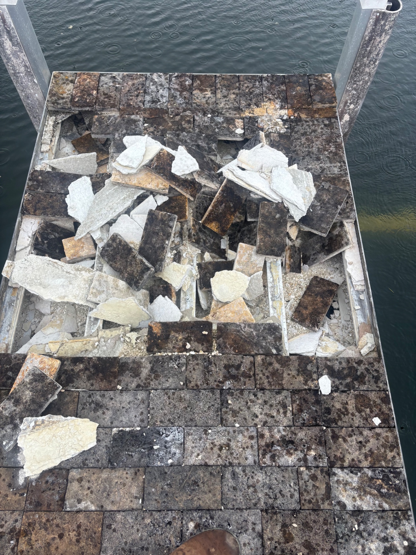 Full rebuild — starting condition. Original paver top has blown apart, thin concrete cap under the pavers cracked and a hole is punched straight through the deck down to the water. Not repairable in place.