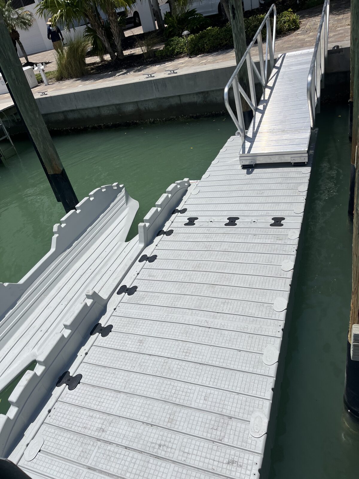 Modular floating dock walkway running along the seawall with cleats every few feet — makes a wide, stable step-down whether the water's high or low.