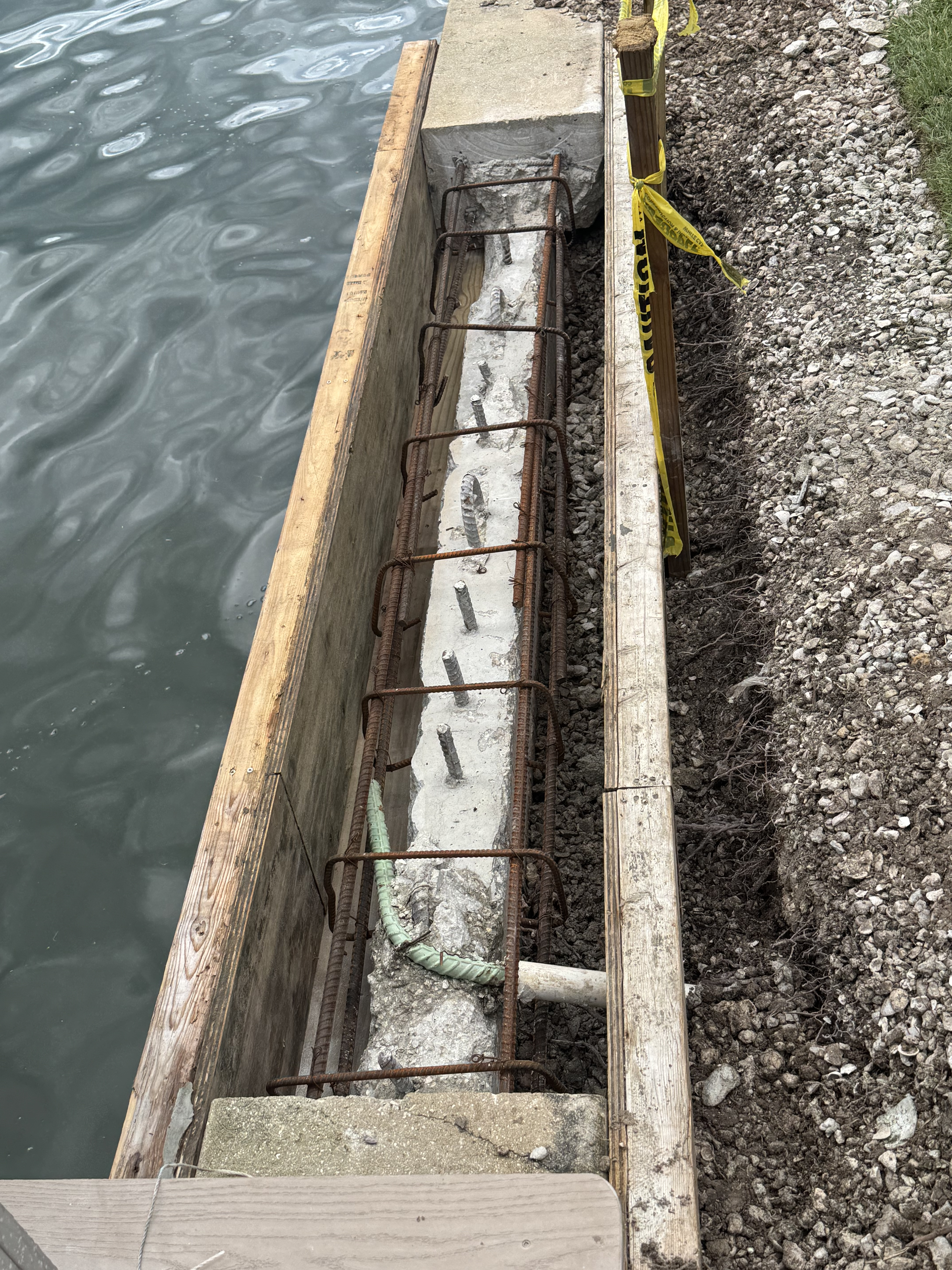Mid-repair: old cap demoed off, new rebar cage tied into the existing wall and formed up along the waterline, ready for a fresh concrete pour to rebuild the cap.